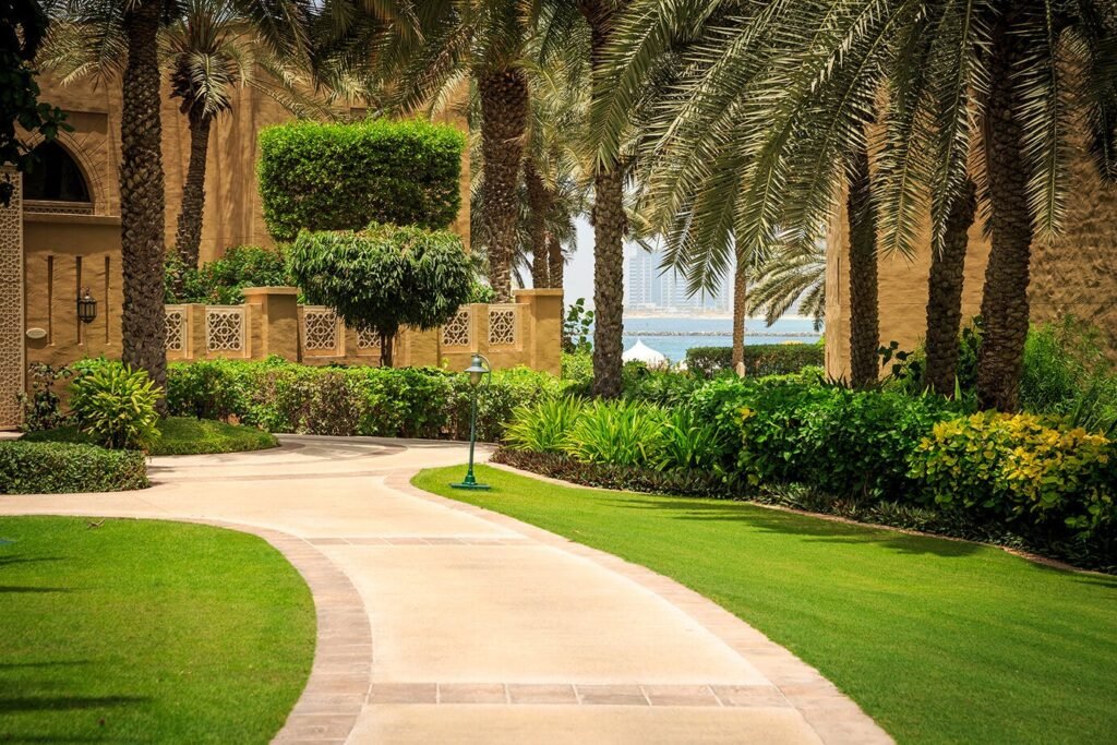 Modern villa landscaping in Dubai, UAE featuring lush green lawn, stone pathways, and elegant garden design with palm trees and lighting